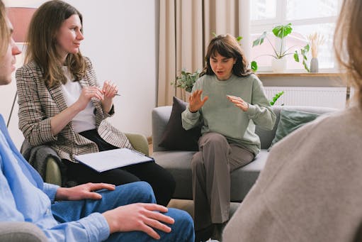 Women in casual clothes sitting on sofa and speaking during group psychotherapy session in cozy office